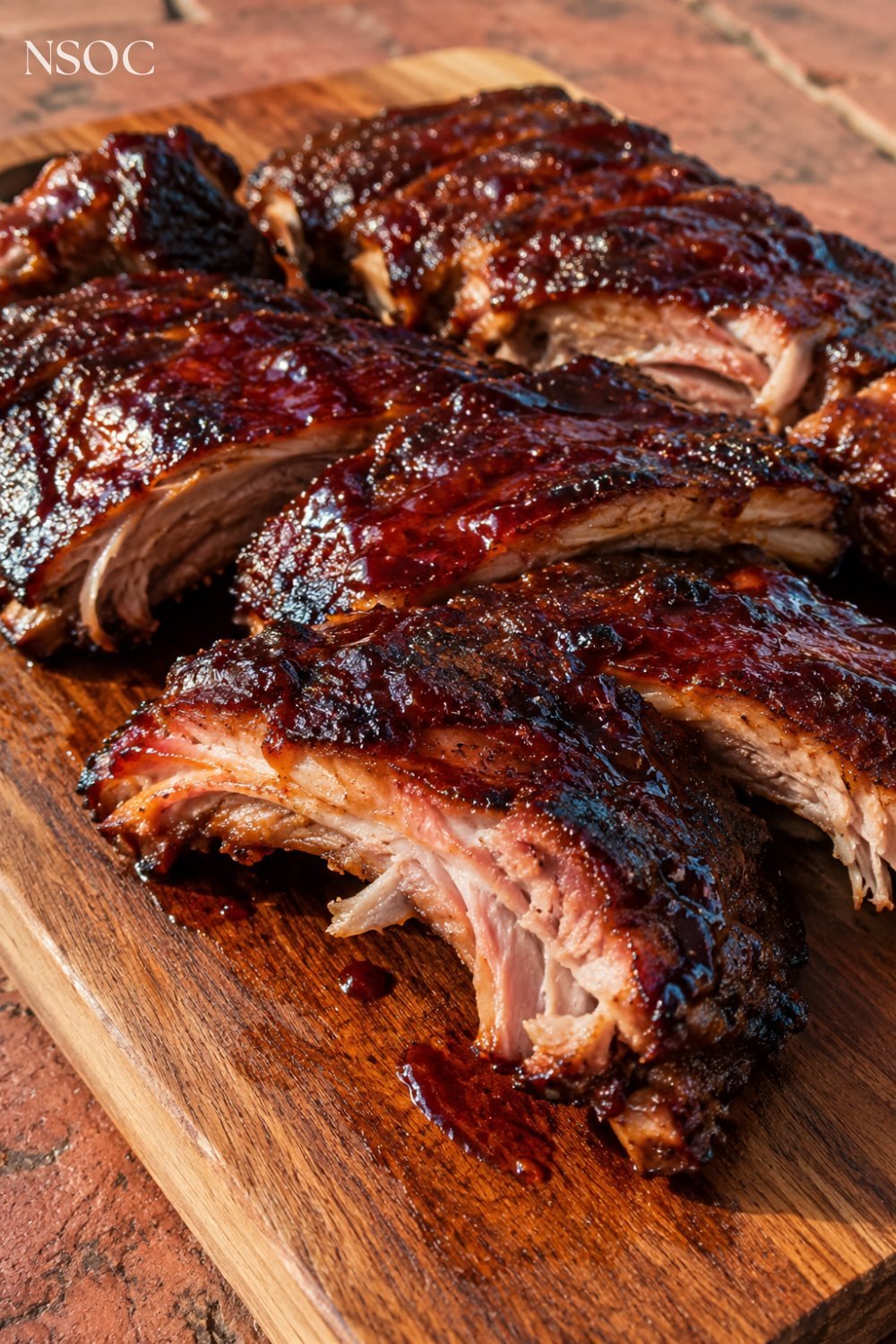 Vertical Pinterest pin of glazed BBQ baby back ribs on a wooden board, an example of NSOC campaign food photography