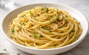 Close-up of glossy aglio e olio pasta twirled on a fork showing golden garlic slices and red pepper flakes clinging to spaghetti strands