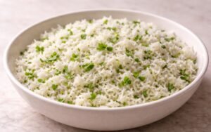 White bowl filled with fluffy jasmine rice mixed with bright green cilantro and lime wedges on the side