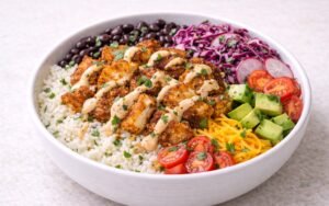 White Fish rice bowl with crispy seasoned white fish, cilantro-lime rice, purple cabbage slaw, black beans, avocado, and chipotle crema drizzle