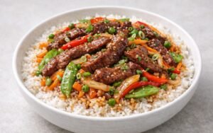 Peking beef stir-fry bowl with glazed flank steak, colorful vegetables, jasmine rice, and sesame seeds