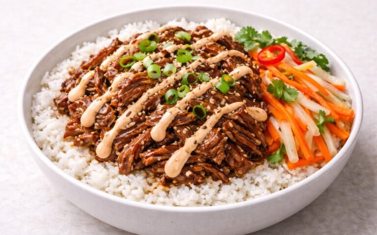 Pulled pork rice bowl with glazed shredded pork, pickled vegetables, sriracha mayo, and sesame seeds over jasmine rice