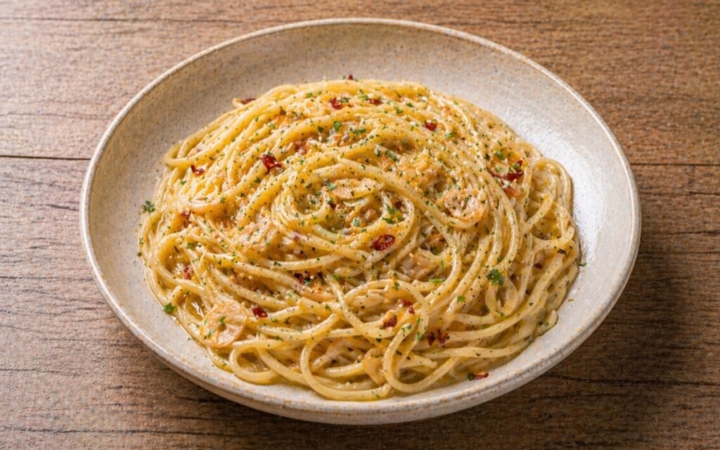 Aglio e olio pasta with glossy olive oil-coated spaghetti, golden garlic slices, red pepper flakes and fresh parsley in a wide white bowl