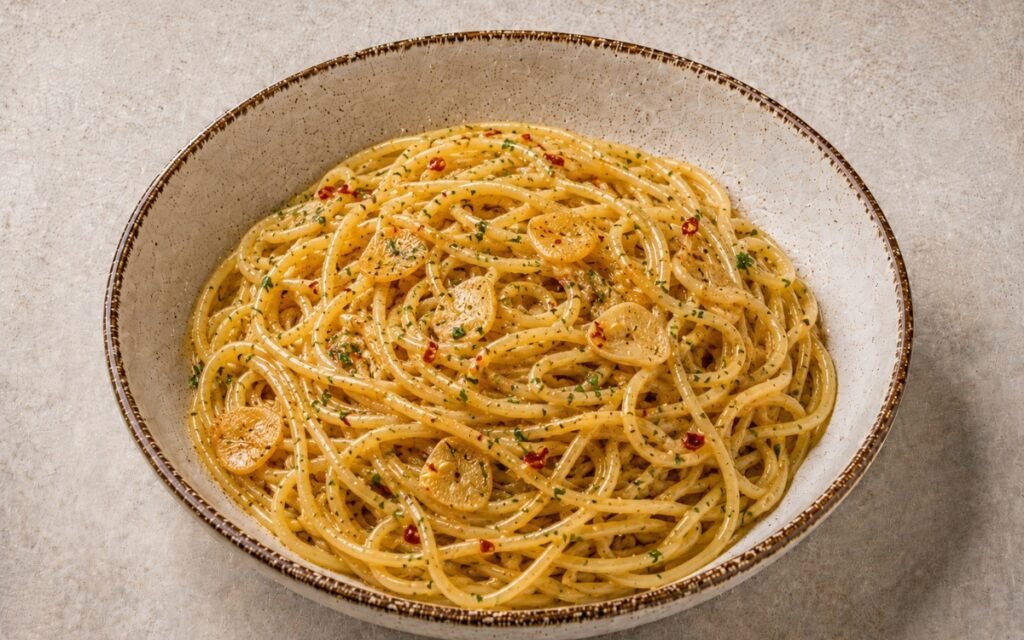 Aglio e olio pasta with glossy olive oil-coated spaghetti, golden garlic slices, red pepper flakes and fresh parsley in a wide white bowl