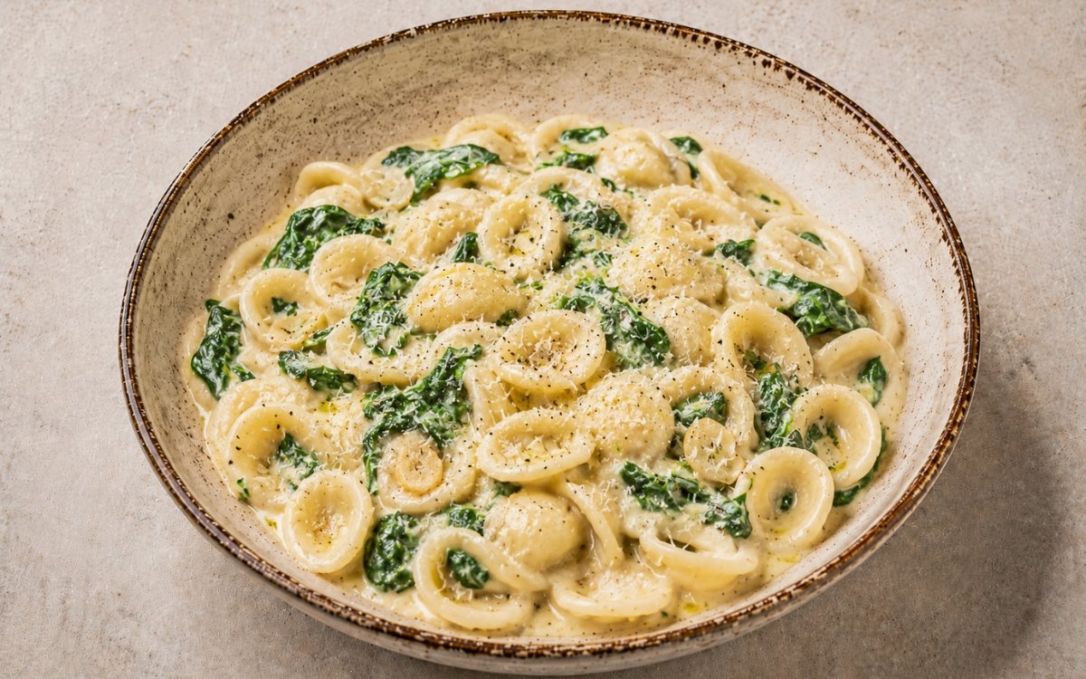 Lemon ricotta spinach orecchiette in a wide white bowl showing cupped orecchiette in creamy lemon ricotta sauce with wilted spinach, Parmigiano, and lemon zest on marble surface