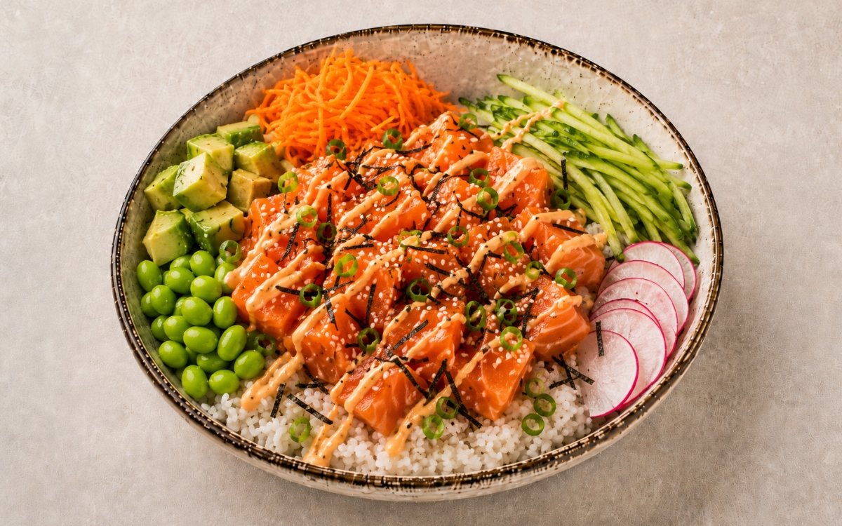 Colorful salmon poke bowl with fresh raw salmon, avocado, edamame, cucumber, and radishes over seasoned sushi rice drizzled with spicy mayo