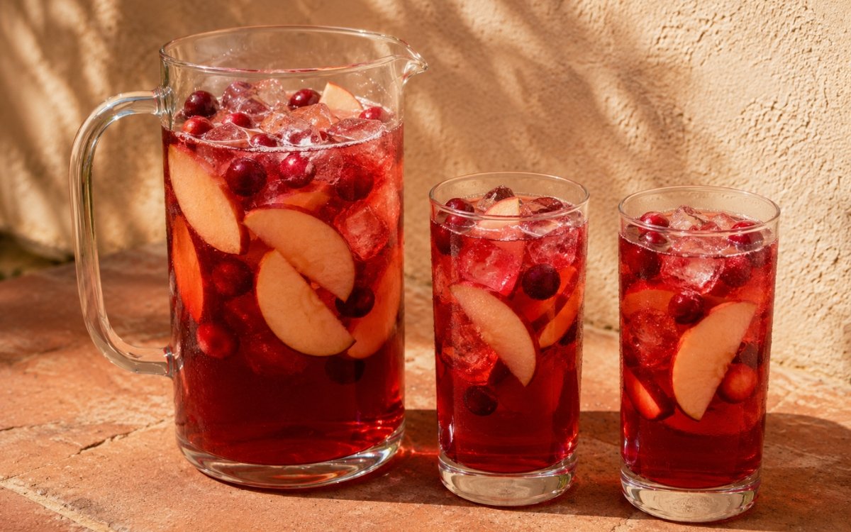 Large apple cranberry pitcher showing vivid deep cranberry-red still drink with apple slices and fresh cranberries visible on marble surface