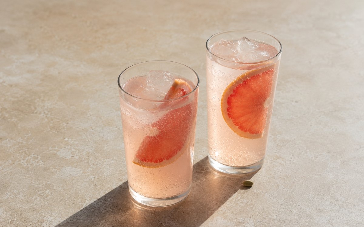 Grapefruit cardamom tonic mocktail in a tall glass showing pale blush sparkling drink over ice with a thick grapefruit slice tucked into the drink on marble surface