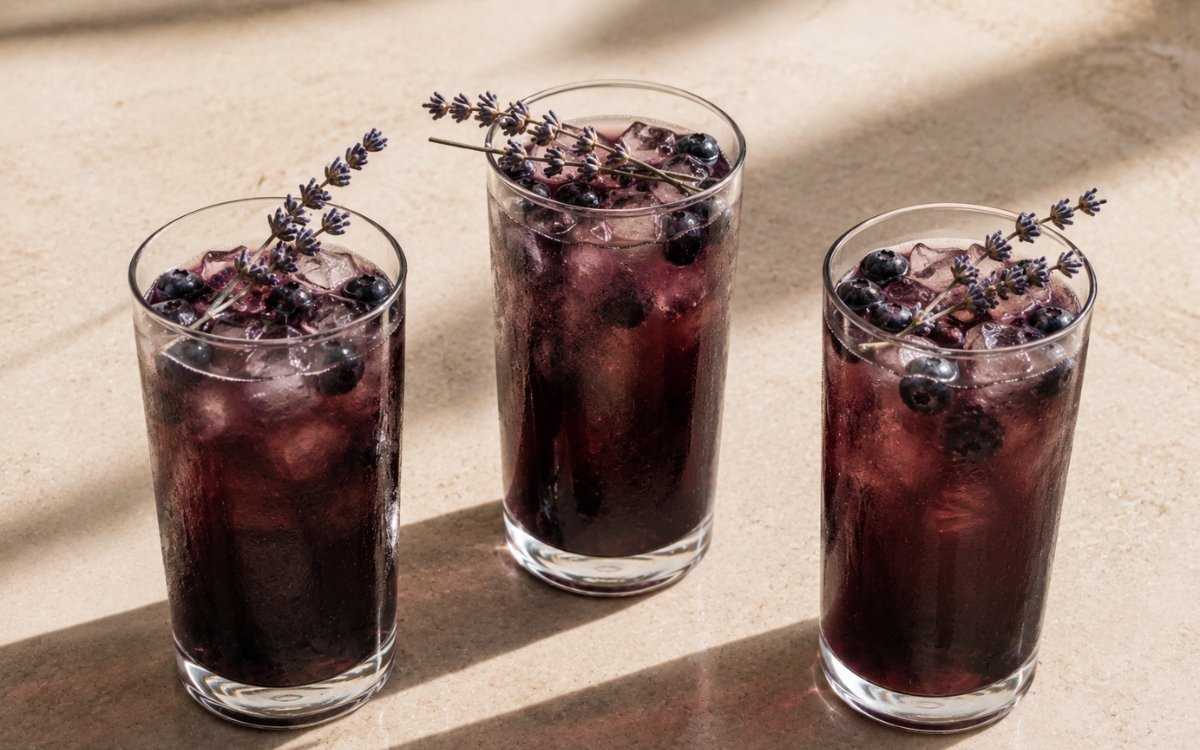 Lavender blueberry iced tea in a tall glass showing deep purple still drink over ice with fresh blueberries and a lavender sprig on marble surface