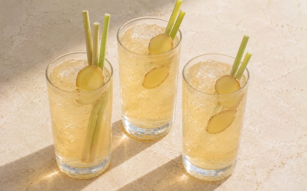 Lemongrass ginger white iced tea in a tall glass showing pale golden still drink over ice with lemongrass segments and thin ginger slices on marble surface