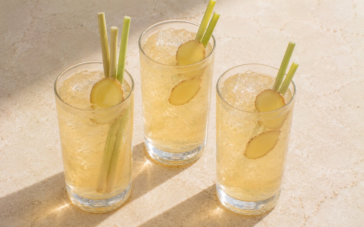 Lemongrass ginger white iced tea in a tall glass showing pale golden still drink over ice with lemongrass segments and thin ginger slices on marble surface