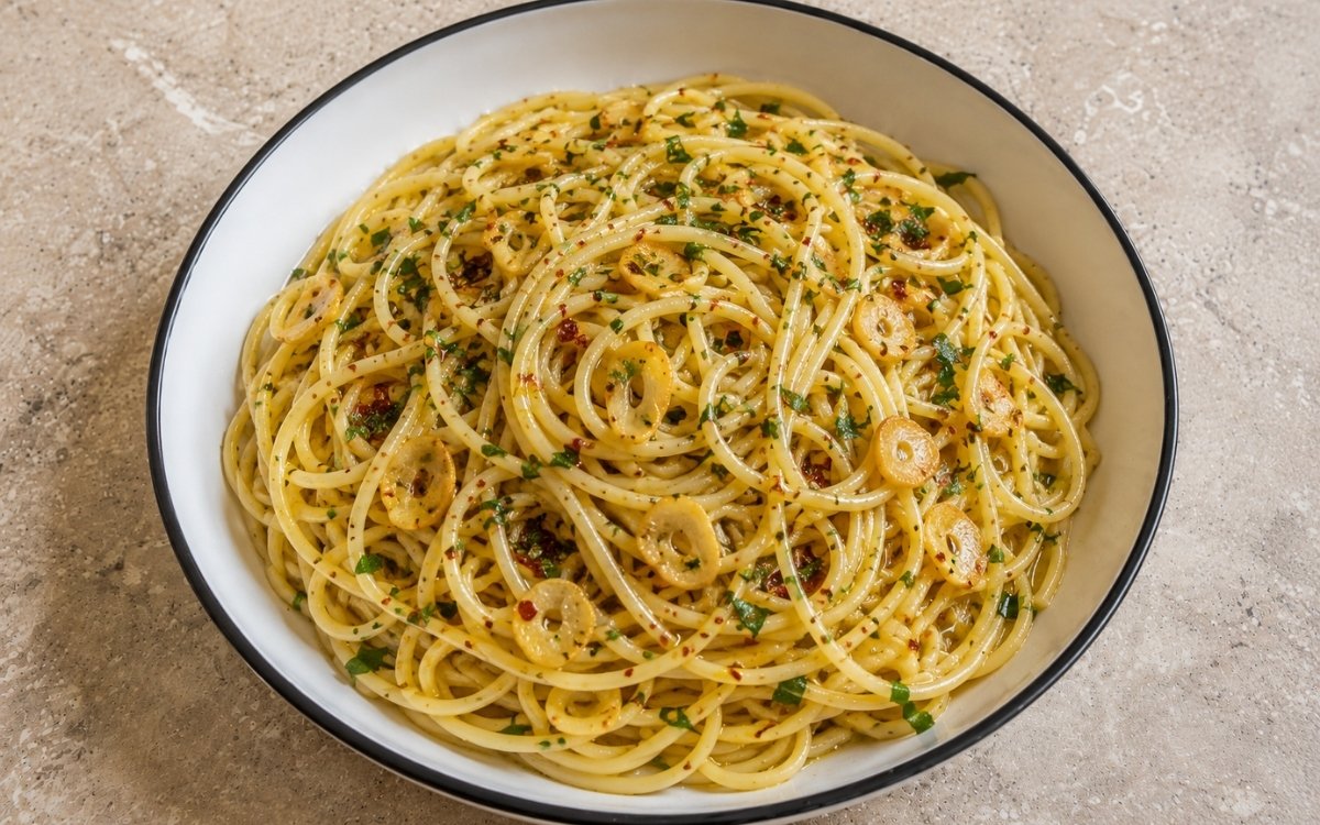 Aglio e olio pasta with spaghetti coated in glossy olive oil, paper-thin golden garlic slices, red pepper flakes and roughly chopped fresh parsley in a white ceramic bowl with black rim