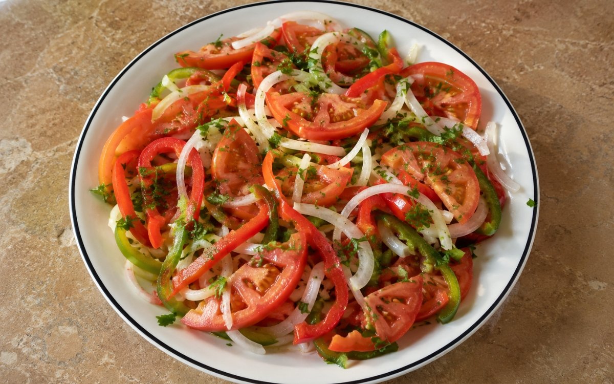 Traditional Argentine criolla salad with sliced tomatoes, onions, and colorful bell peppers on serving platter