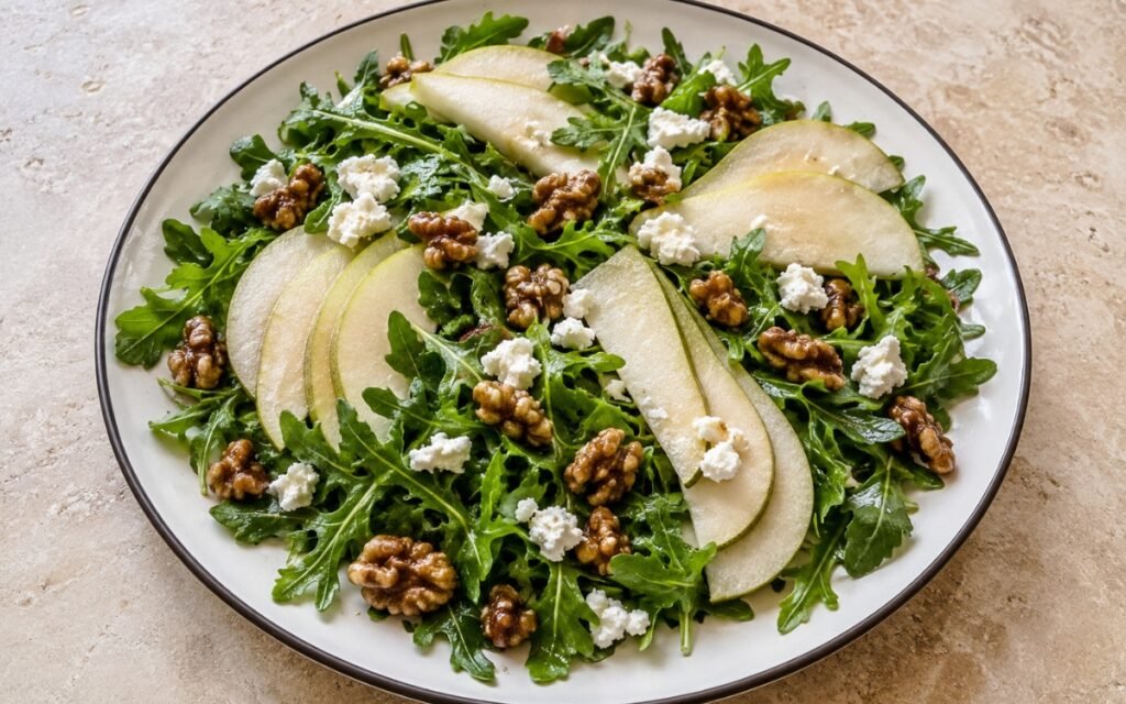 Plate of arugula pear salad with sliced pears, goat cheese crumbles, and candied walnuts