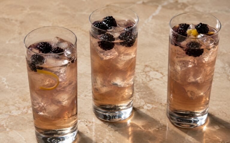 Blackberry jasmine iced tea in a tall glass showing deep purple-red still drink over ice with fresh blackberries on marble surface
