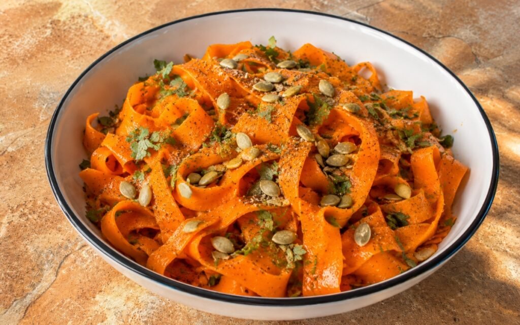 Carrot cumin side salad with ribboned carrots, toasted cumin dressing, and pumpkin seeds in a white bowl