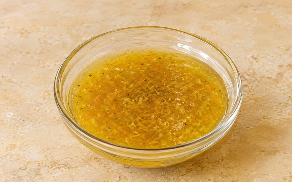 Citrus olive oil dressing in a small glass bottle showing golden dressing with visible citrus zest flecks