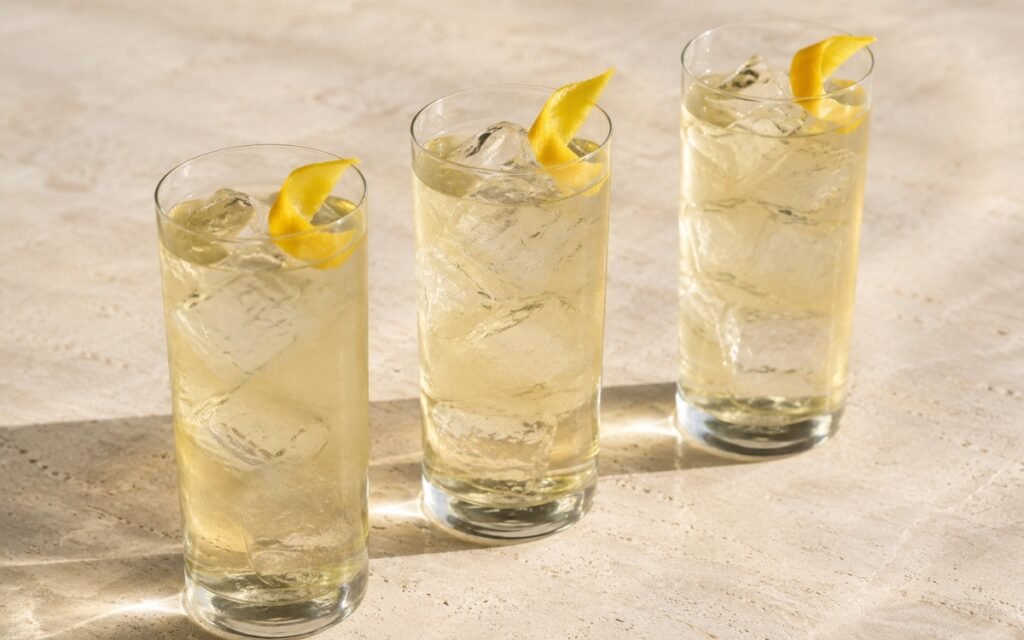 Cold brew white tea in a tall glass showing very pale clear still drink over ice with a lemon peel twist on marble surface
