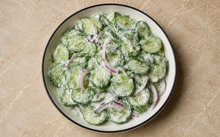 Bowl of creamy cucumber salad with fresh dill and red onions on a white plate