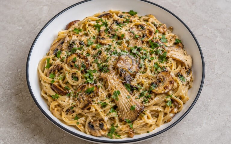Creamy mushroom garlic pasta with pappardelle in pale amber cream sauce with golden-brown cremini, shiitake and oyster mushrooms, garlic, fresh parsley and Parmigiano-Reggiano in a white ceramic bowl with black rim