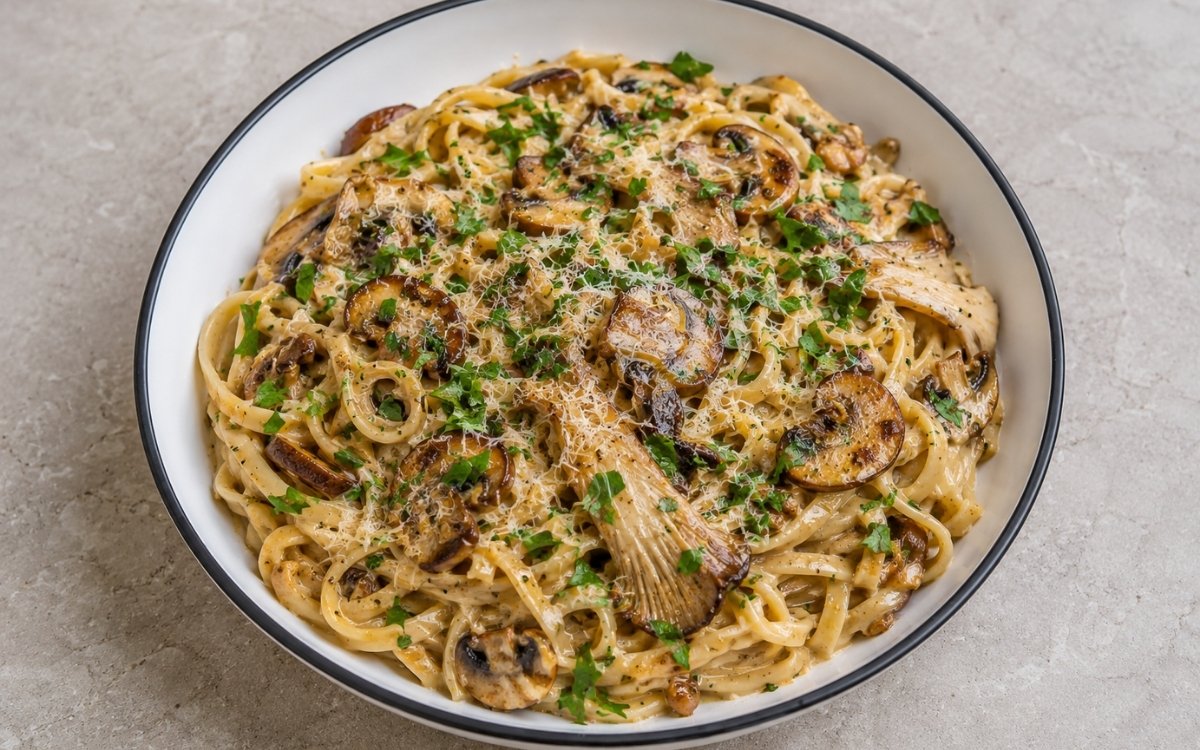 Creamy mushroom garlic pasta with pappardelle in pale amber cream sauce with golden-brown cremini, shiitake and oyster mushrooms, garlic, fresh parsley and Parmigiano-Reggiano in a white ceramic bowl with black rim