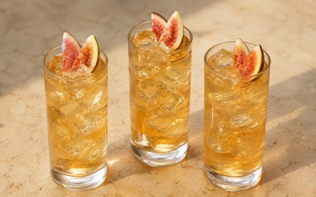 Fig jasmine iced tea in a tall glass showing pale amber-pink still drink over ice with fresh fig halves on marble surface
