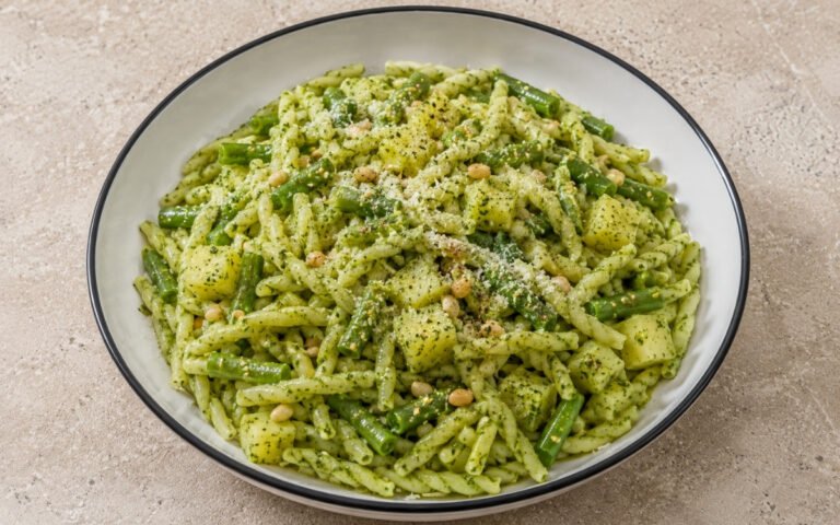 Basil pesto pasta with trofie coated in vivid green pesto with pine nuts, green beans and Yukon Gold potato cubes, Parmigiano-Reggiano and black pepper in a white ceramic bowl with black rim