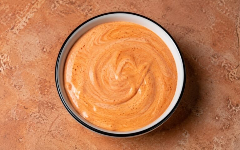 Harissa yogurt sauce in a white bowl showing pale orange-pink creamy sauce with swirl of harissa
