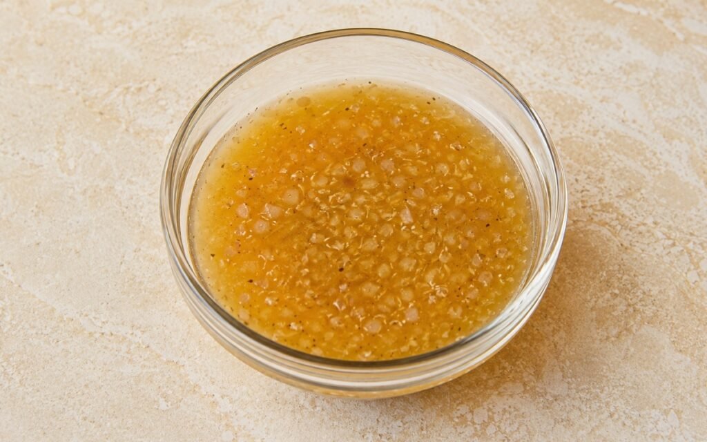 Honey shallot vinaigrette in a small glass pitcher showing golden dressing with visible shallot flecks