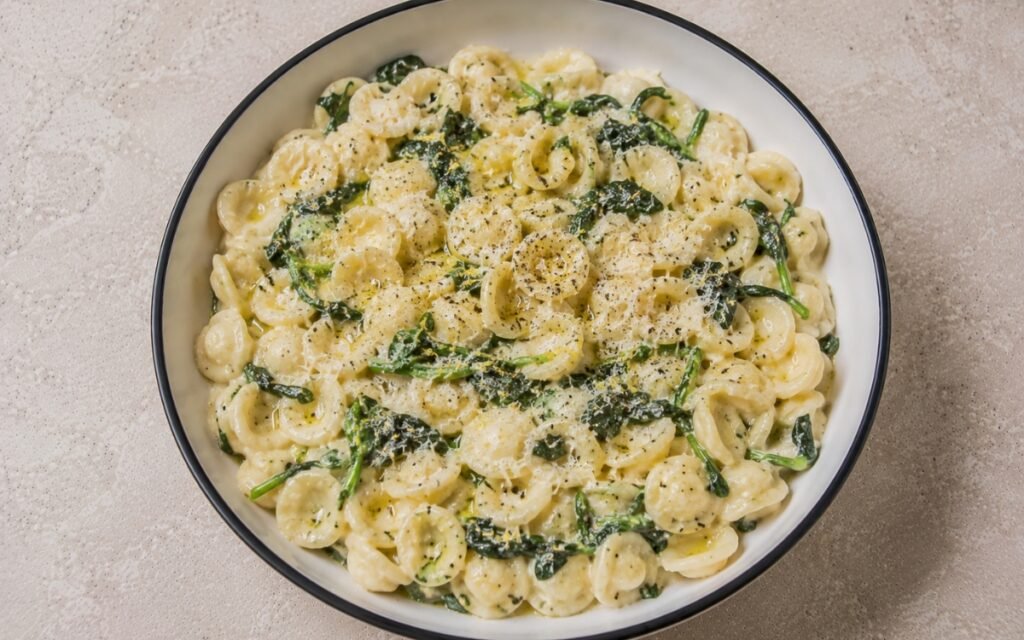 Lemon ricotta spinach orecchiette in creamy pale ivory ricotta-lemon sauce with wilted baby spinach, lemon zest, Parmigiano-Reggiano and black pepper in a white ceramic bowl with black rim