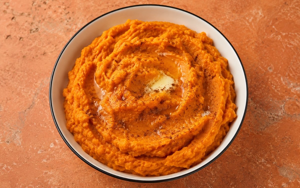Creamy mashed sweet potatoes in a white bowl with butter melting on top