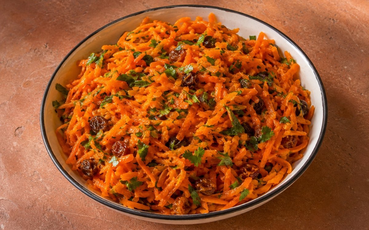 Moroccan carrot salad in a white bowl with grated carrots, fresh herbs, raisins, and toasted almonds