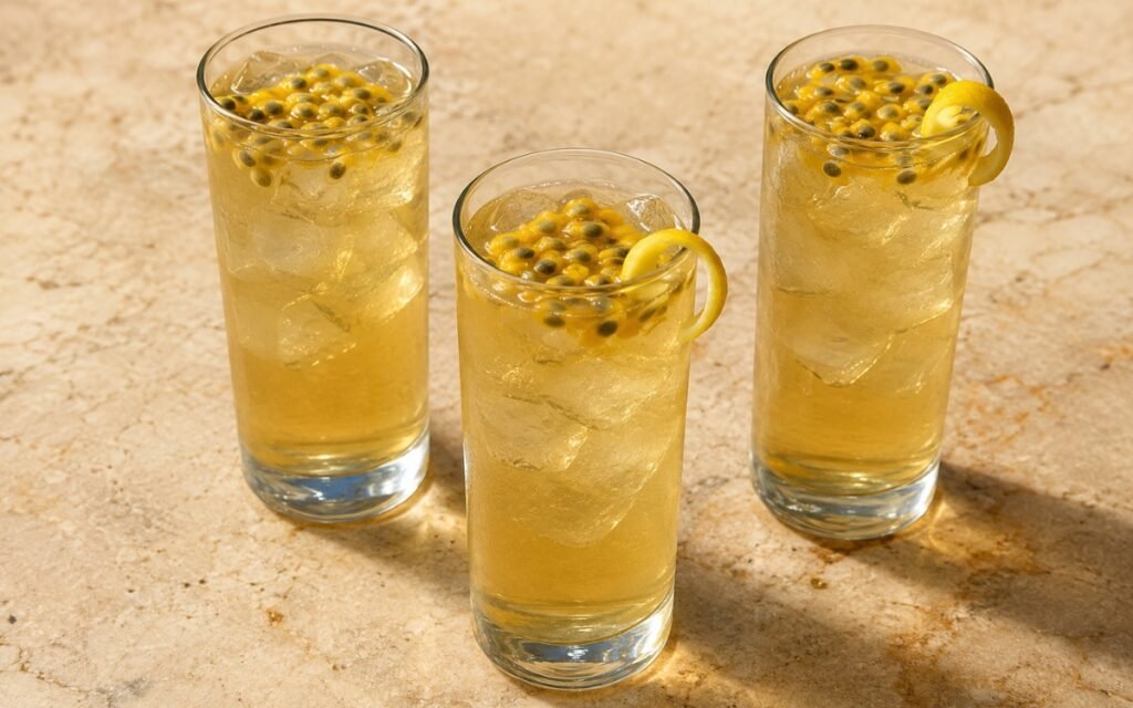 Passion fruit white iced tea in a tall glass showing pale golden still drink over ice with passion fruit pulp and a lemon peel twist on marble surface