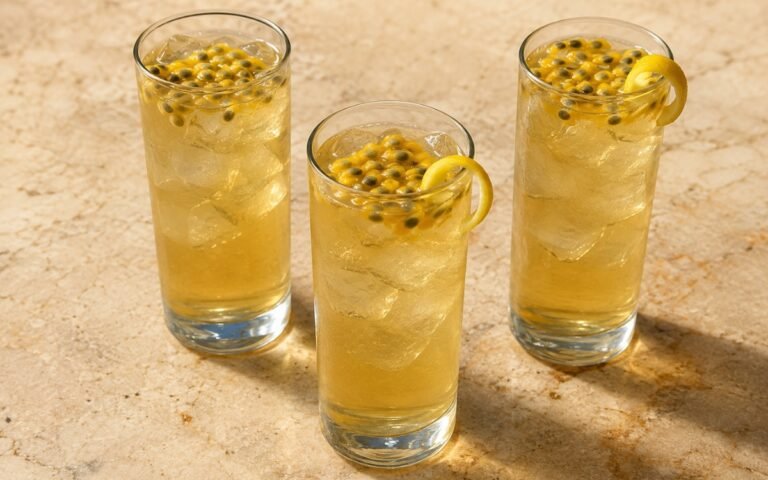 Passion fruit white iced tea in a tall glass showing pale golden still drink over ice with passion fruit pulp and a lemon peel twist on marble surface