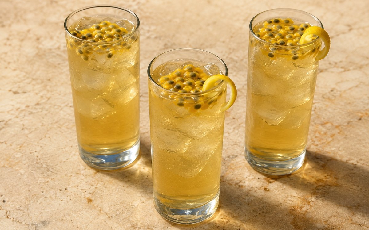 Passion fruit white iced tea in a tall glass showing pale golden still drink over ice with passion fruit pulp and a lemon peel twist on marble surface