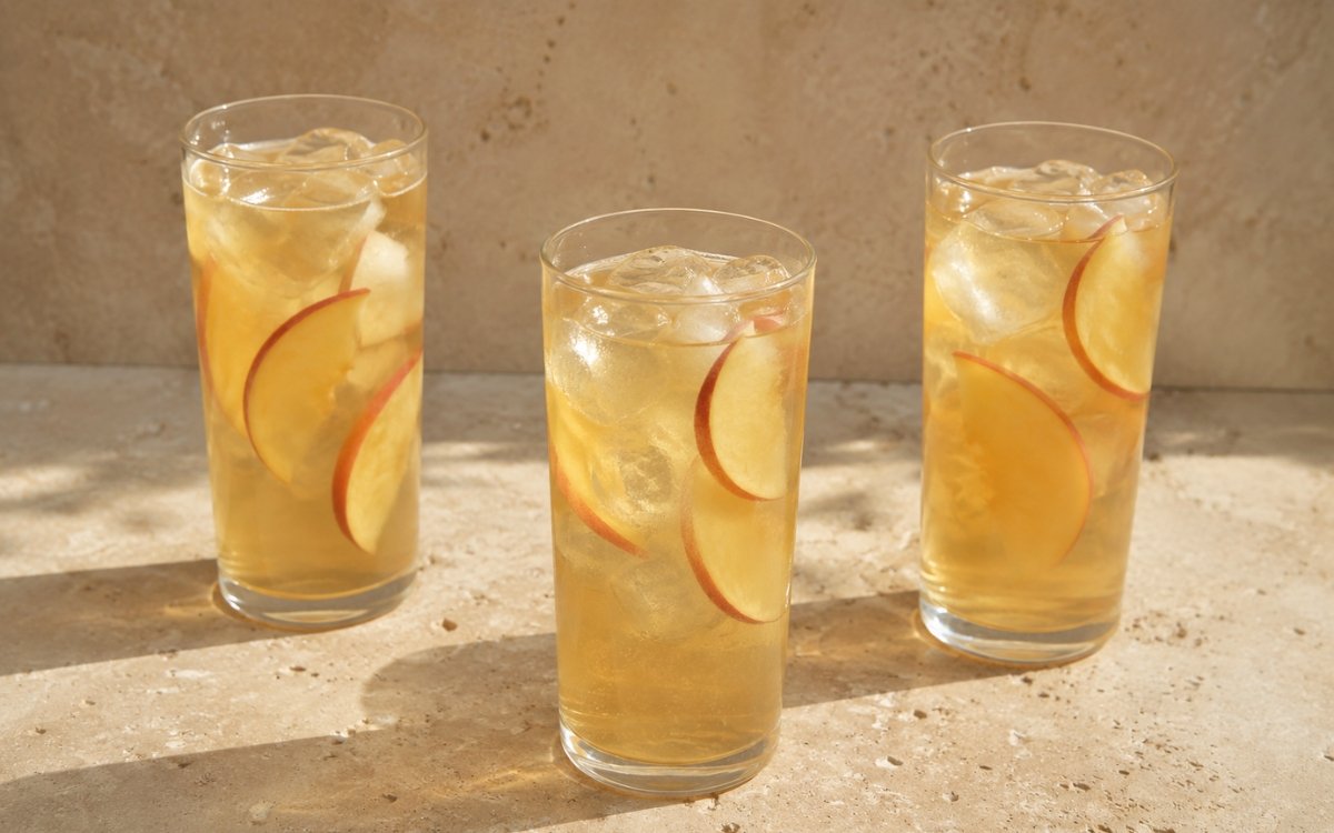 Peach jasmine iced tea in a tall glass showing pale golden still drink over ice with fresh peach slices on marble surface