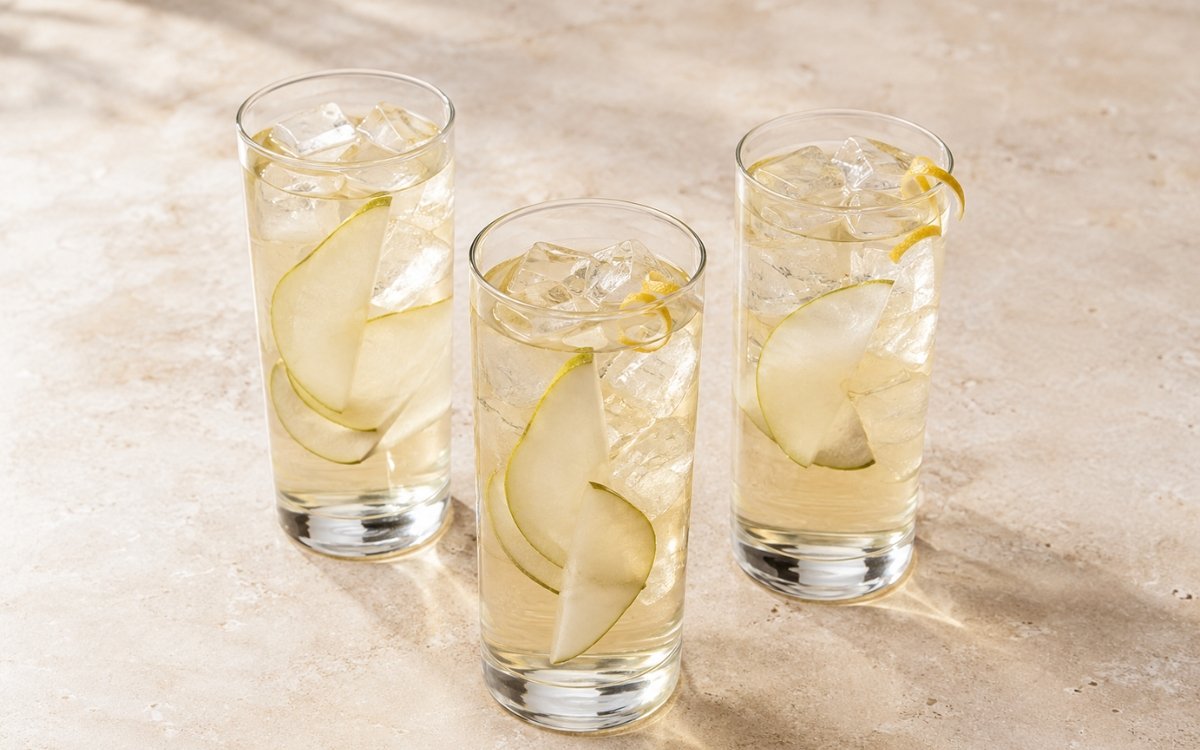 Pear white iced tea in a tall glass showing very pale clear still drink over ice with thin pear slices on marble surface