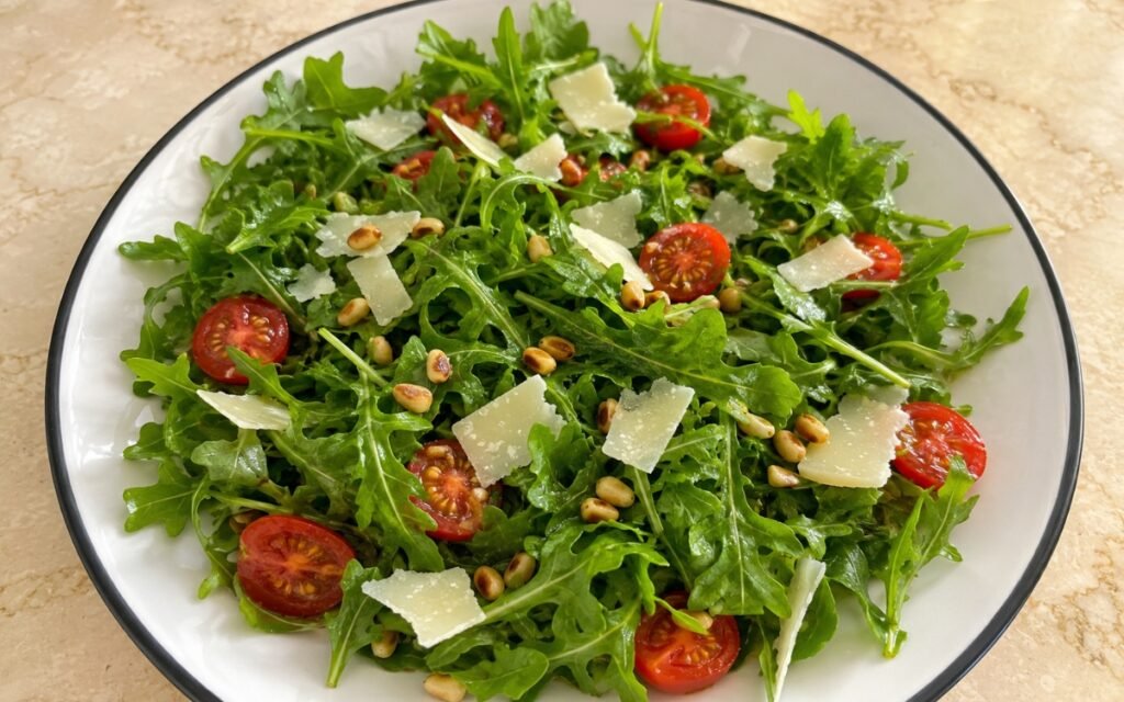 Simple arugula salad with cherry tomatoes, shaved Parmesan, and pine nuts on a white plate