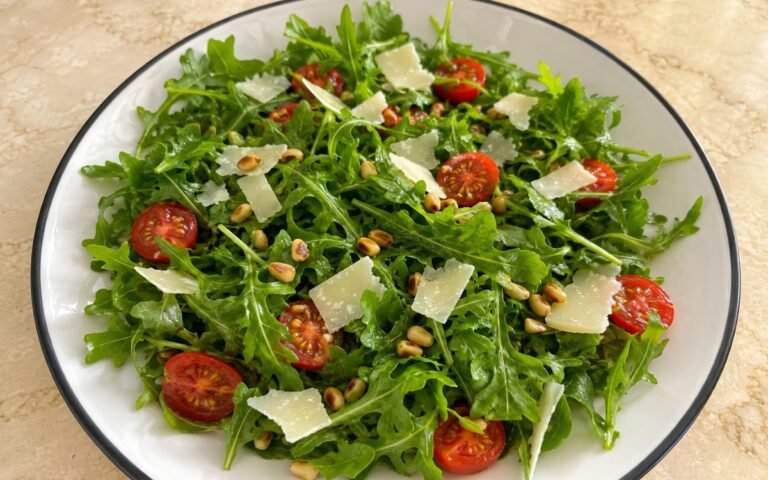 Simple arugula salad with cherry tomatoes, shaved Parmesan, and pine nuts on a white plate
