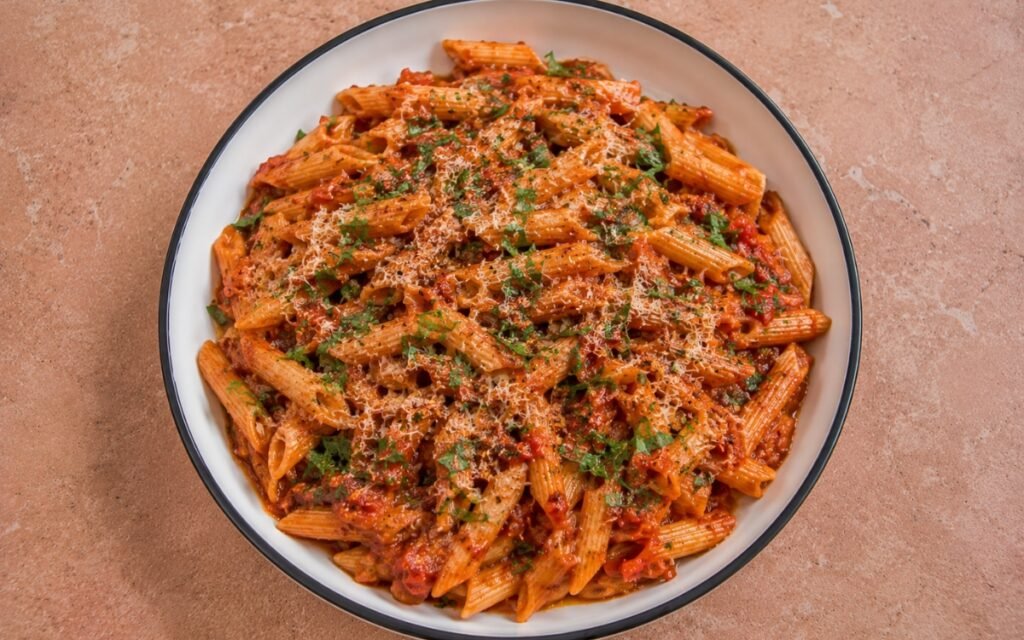 Spicy Calabrian chili penne arrabbiata in vivid deep red arrabbiata sauce with Calabrian chili paste, red pepper flakes, fresh parsley and Parmigiano-Reggiano in a white ceramic bowl with black rim