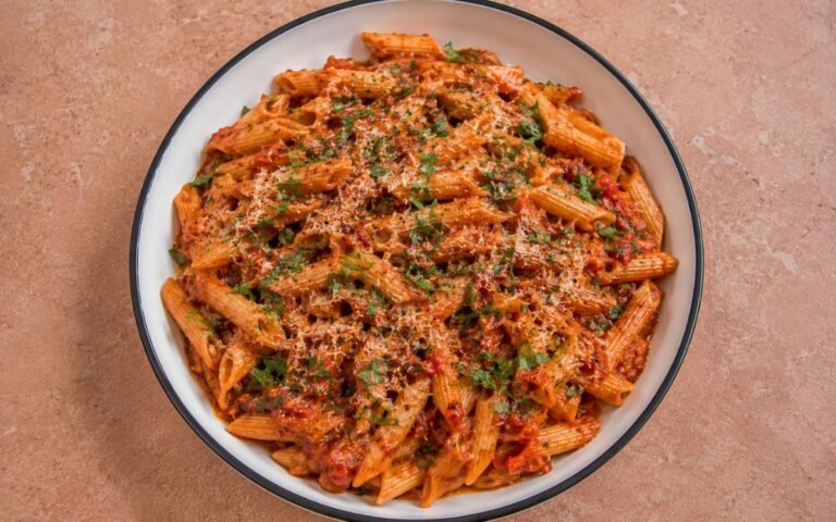 Spicy Calabrian chili penne arrabbiata in vivid deep red arrabbiata sauce with Calabrian chili paste, red pepper flakes, fresh parsley and Parmigiano-Reggiano in a white ceramic bowl with black rim