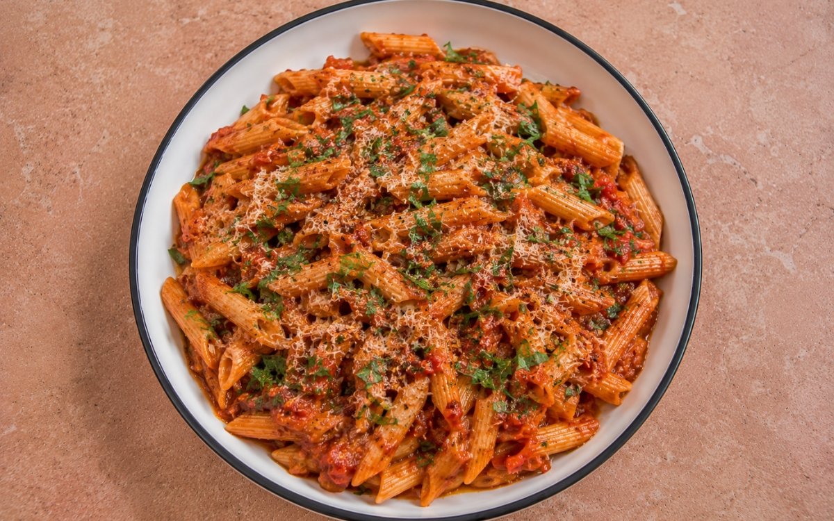 Spicy Calabrian chili penne arrabbiata in vivid deep red arrabbiata sauce with Calabrian chili paste, red pepper flakes, fresh parsley and Parmigiano-Reggiano in a white ceramic bowl with black rim