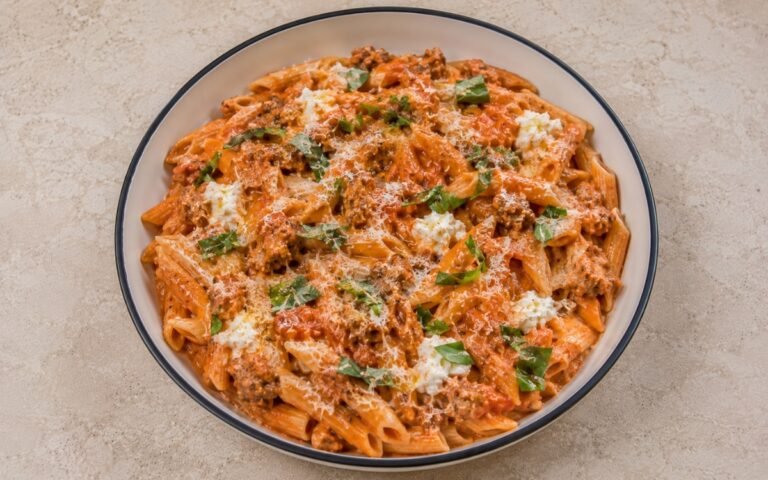 Tomato pasta with ricotta and Italian sausage with fusilli in silky pale pink-red tomato-ricotta sauce, crumbled browned Italian sausage, torn basil and Parmesan in a white ceramic bowl with black rim