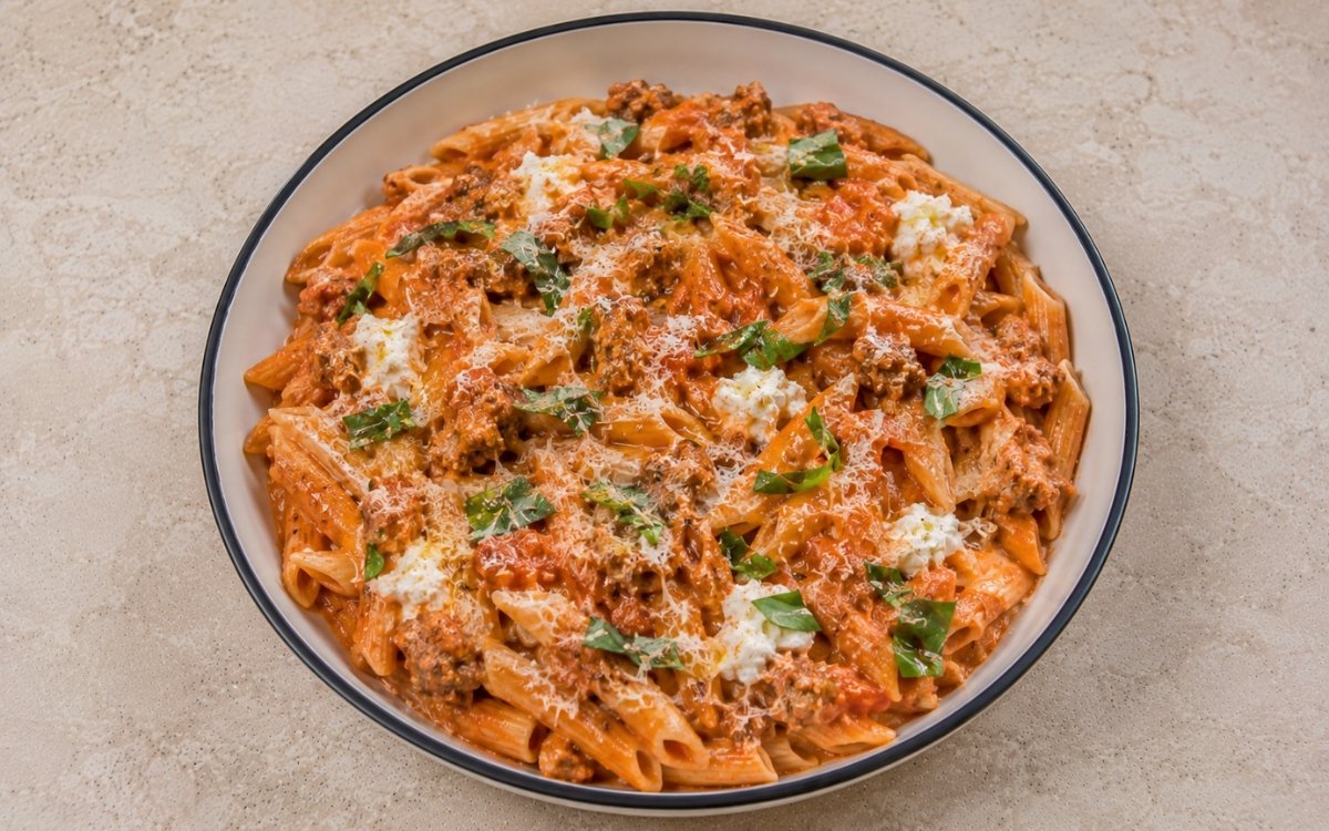 Tomato pasta with ricotta and Italian sausage with fusilli in silky pale pink-red tomato-ricotta sauce, crumbled browned Italian sausage, torn basil and Parmesan in a white ceramic bowl with black rim