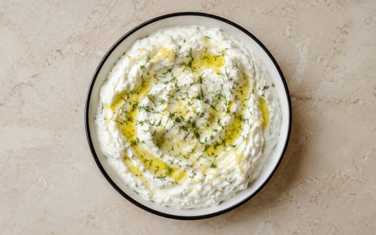 Bowl of fluffy white whipped feta sauce with olive oil drizzle and fresh dill