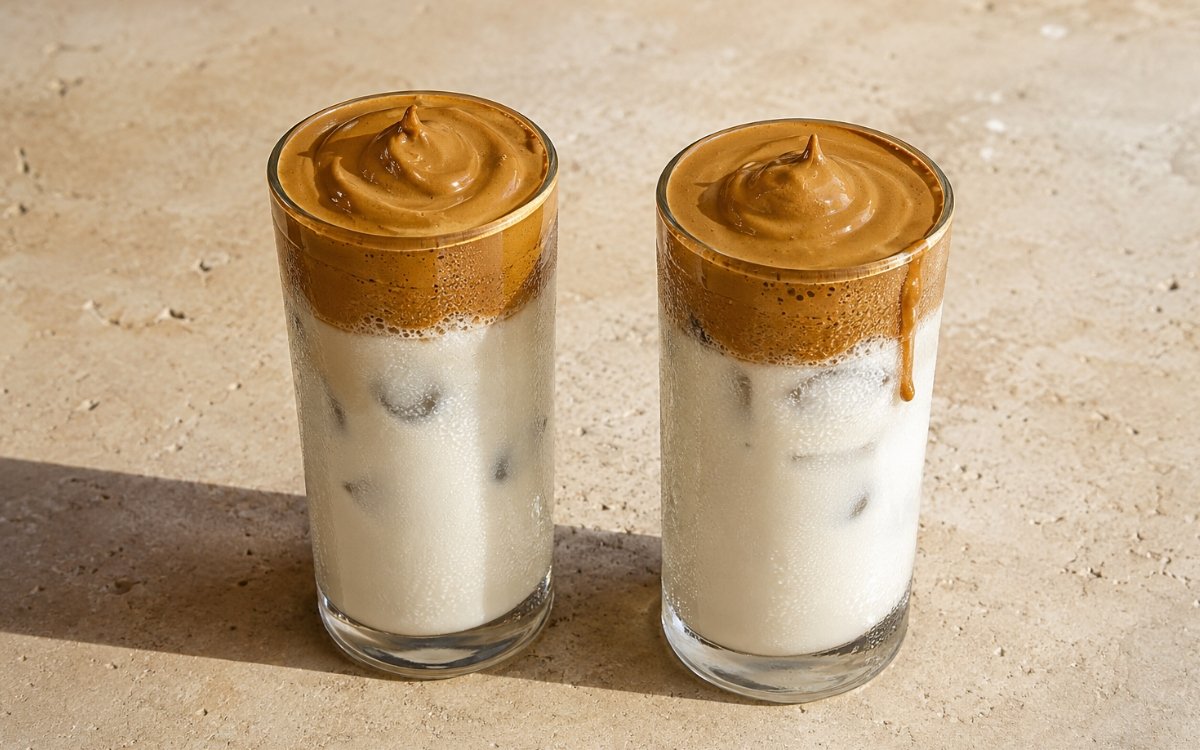 Dalgona whipped coffee in a glass showing a thick, dense golden-brown coffee foam sitting distinctly above cold milk and ice, on marble surface