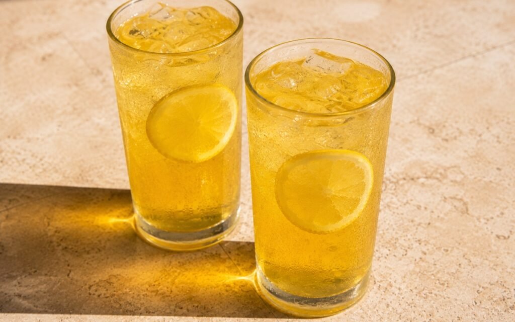 glasses of golden honey lemonade with thin lemon wheels floating in ice, on marble surface