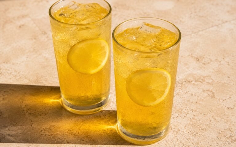 glasses of golden honey lemonade with thin lemon wheels floating in ice, on marble surface