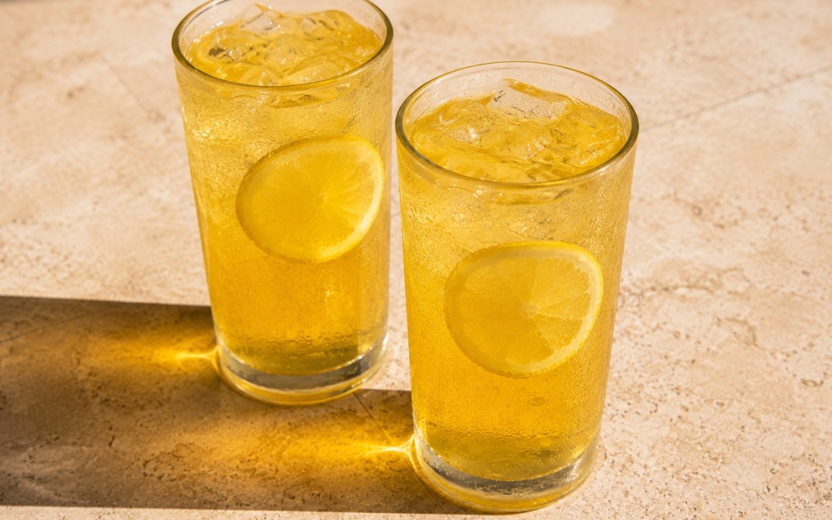 glasses of golden honey lemonade with thin lemon wheels floating in ice, on marble surface