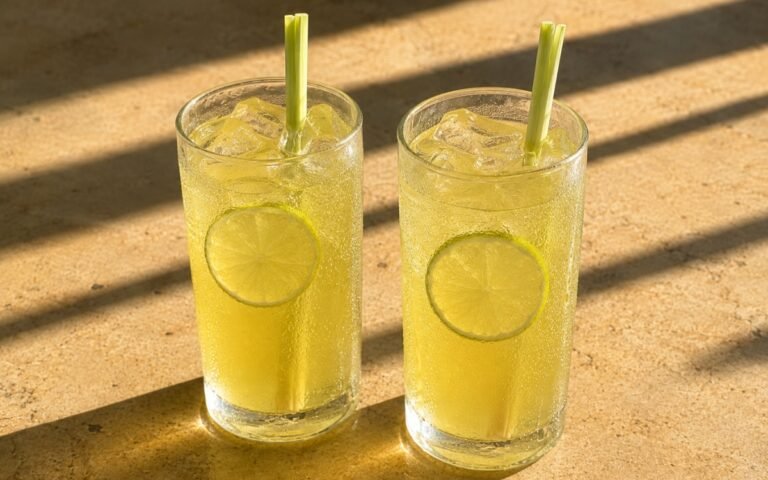 glasses of lemongrass lime green tea cooler with lime wheels and standing lemongrass stalks, on marble surface
